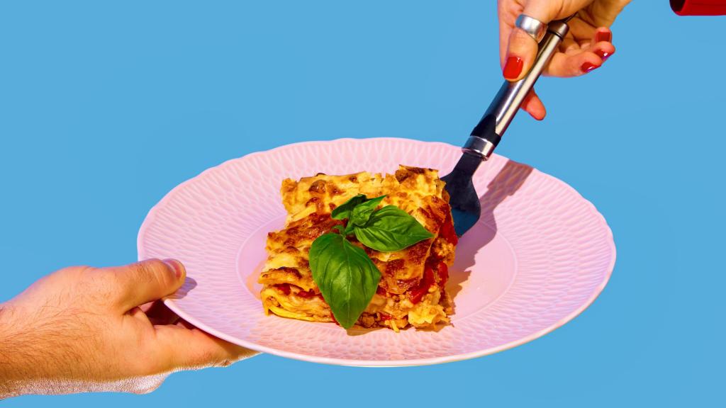 Una mano coge un trozo de lasaña del plato de otra persona.